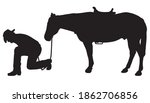 A cowboy is kneeling and studying the ground while his horse waits