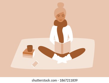 Coziness concept in the winter. Beautiful woman with winter socks and scarf reading a book with more books, coffee mug and cellphone on the carpet near her. 