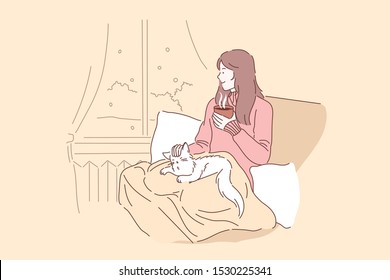 Cozy, relax, dream concept. Young woman or girl enjoys the comfort of sitting on a chair with a blanket and caressing her pet cat. Thoughtful lady in looks out the window and drinks tea or coffee.