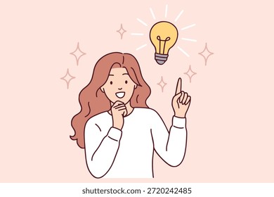 Creative girl finds smart solution or startup idea. Smiling woman points up at lightbulb symbol representing inspiration and intelligence in professional work process.