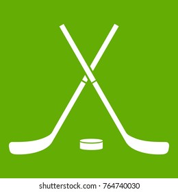 Crossed hockey sticks and puck icon white isolated on green background. Vector illustration