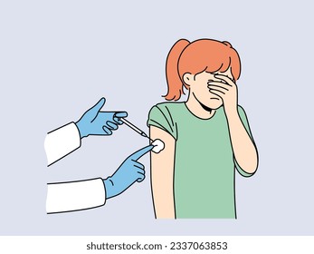 Crying little girl is afraid of injections and closes eyes during injection in shoulder and vaccination against measles or flu. Hands of doctor with syringe making injection to child