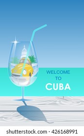 Cuba travel symbols - capitol, old car, palms - in the cocktail glass standing on the 
wooden cracked table on the turquoise ocean background 