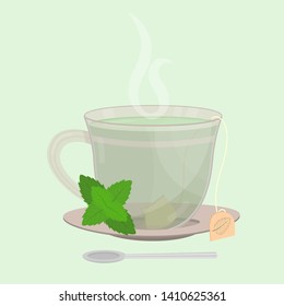 Cup of mint tea. Tea sachet with mint branch on the saucer. Smoke on the drink. Spoon in front of cup.