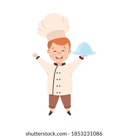 Cute Boy Chef Cook Holding Round Cloche Tray, Smiling Kid in Chef Uniform Cooking in Kitchen Cartoon Style Vector Illustration