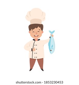 Cute Boy Chef Cooking Fresh Fish, Smiling Kid in Chef Uniform Cooking in Kitchen Cartoon Style Vector Illustration