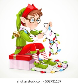 Cute boy elf sitting on a box with a gift and unravels a Christmas garland isolated on white background