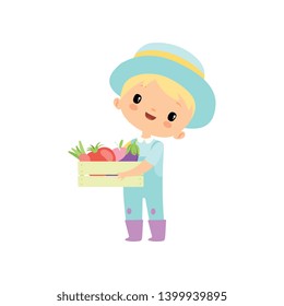 Cute Boy in Overalls, Rubber Boots and Hat Holding Wooden Box Full of Vegetables, Young Farmer Cartoon Character Engaged in Agricultural Activities Vector Illustration