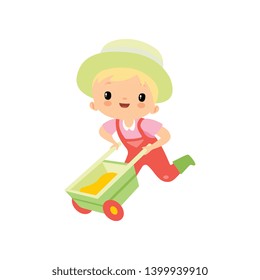 Cute Boy in Overalls, Rubber Boots and Hat Pushing Wheelbarrow, Young Farmer Cartoon Character Engaged in Agricultural Activities Vector Illustration