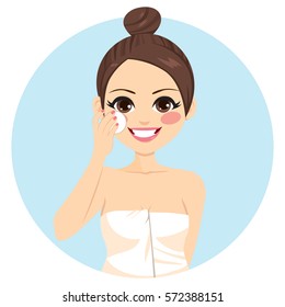 Cute brunette woman with hair bun cleaning face with white cotton pad