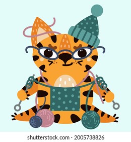 Cute cartoon striped tiger. Vector illustration isolated on white background. The cat with glasses knits. A sly kitten in a hat with woolen balls. Flat style, childish print.