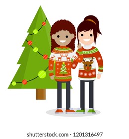 A cute couple girl friend in winter sweaters with a pattern stand hugging about a decorated garland and a Christmas tree light. Woman and girl celebrate Christmas and new year.
