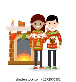A cute couple in red sweaters with a pattern celebrates new year and Christmas. Fireplace, candles and socks for gifts. Happy multicultural family and holiday. Deer and snow