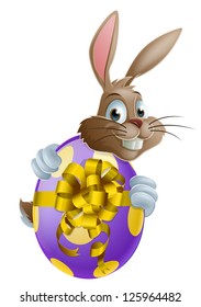 Cute Easter bunny cartoon character holding onto and peeking round a painted chocolate Easter egg