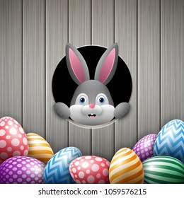 Cute Easter bunny peeking out of a hole with colorful eggs