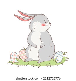 A cute fluffy rabbit in a field with Easter eggs looks around. Vector illustration of a chubby hand drawn grey white bunny looking for easter eggs. Cartoon style design.
