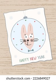 Cute funny bunny hand-drawn on a Christmas ball. Handwritten inscription Happy New Year. Year of the Rabbit in the Chinese calendar. Greeting card on a wooden table. Cartoon style.
