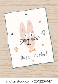 Cute funny Easter Bunny with lettering Happy Easter. Handwritten text. Painted Easter eggs and stars around it. Greeting Card on a wooden table. Template, write your own inscription.