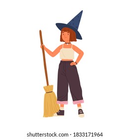 Cute girl in witch hat standing with a broomstick. Portrait of funny little wizard or sorcerer holding magic broom. Young female mage with red hair. Flat vector cartoon illustration isolated on white