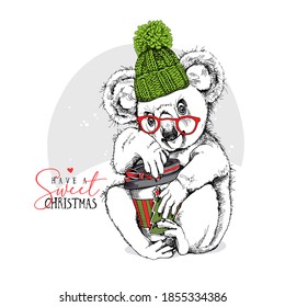 Cute Koala in the knitted hat, glasses and with a plastic cup of coffee. Merry Christmas and New year card, Humor composition, hand drawn style print. Vector illustration.