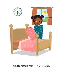 cute little African girl making bed arranging pillow and bed cover neat doing her housework chores in the morning at home