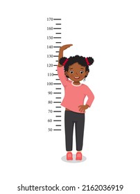 Cute little African girl measuring height of her growth on the background of wall