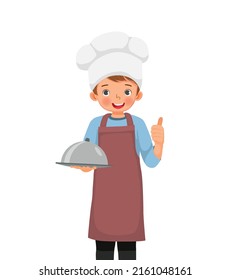 cute little boy in chef hat and apron holding a tray showing thumb up