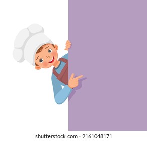 cute little boy in chef hat and apron peeking from board pointing finger to empty banner for copy space