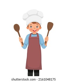 cute little boy in chef hat and apron holding cooking utensil spatula and ladle spoon