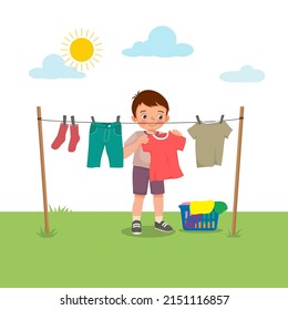 Cute little boy doing laundry chore hanging wet clothes outside under sunlight to dry on the backyard