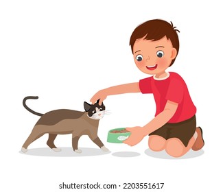 Cute little boy feeding his pet cat with animal food at home