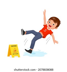 Cute little boy having accident slipping on wet floor and falling down near yellow caution sign.