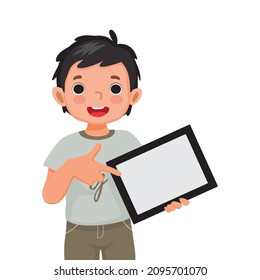 cute little boy holding digital tablet with finger pointing to empty screen or copy space for texts, messages and advertising content. Kids and electronic gadget devices concept for children.

