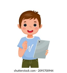 cute little boy holding and using digital tablet touching screen browsing internet, doing homework, and playing games. Kids and electronic gadget devices concept for children.