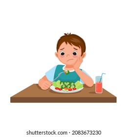 Cute little boy picky eater frustrating looking at broccoli with no appetite and refusing to eat vegetables.