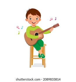 Cute little boy playing a guitar and singing sitting on a wooden chair