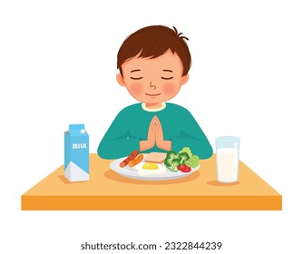 Cute little boy praying before eating breakfast at the table