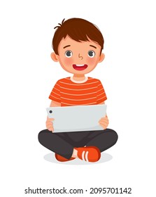 Cute little boy sitting on floor using digital tablet touching screen browsing internet, doing homework, and playing games. Kids and electronic gadget devices concept for children.