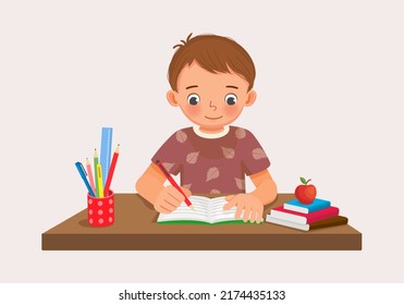 Cute little boy sitting on the desk studying writing on notebook doing her homework at home