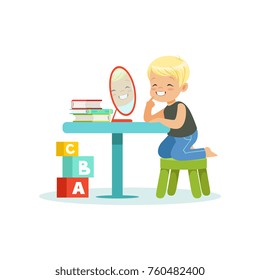 Cute little boy sitting at the table, looking at his reflection in mirror and doing pronunciation exercises