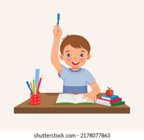 Cute little boy student rising hand answering question sitting at his desk in the classroom