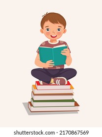 cute little boy student sitting cross legged on stack of books reading