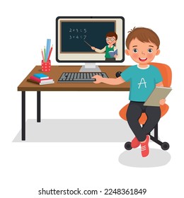 Cute little boy studying from home via Internet video conference with teacher using computer desktop