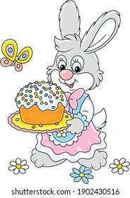 Cute little bunny in a beautiful holiday dress holding a dish with a sweet Easter cake colorfully decorated with candies, vector cartoon illustration isolated on a white background