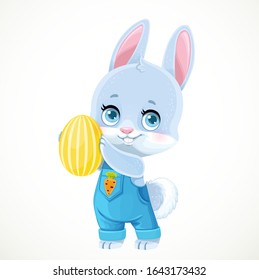 Cute little bunny in denim overalls holds yellow Easter painted egg in paws isolated on white background
