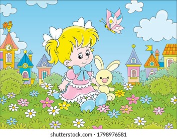 Cute little girl in a beautiful pink dress sitting with a small toy rabbit among flowers on a green lawn against a background of colorful houses of a small town, vector cartoon illustration