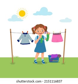 Cute little girl doing laundry chore hanging wet clothes outside under sunlight to dry on the backyard