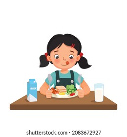 Cute Little Girl Feeling Excited Eating Breakfast With Bread, Fried Egg, Broccoli, Vegetables, Glass Of Milk Holding Spoon And Fork.