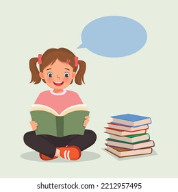 Cute little girl reading a book sitting on the floor beside stack of books