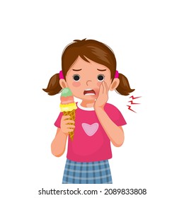 Cute little girl with sensitive teeth has a toothache while eating cold ice cream touching her cheek and feel aching and pain